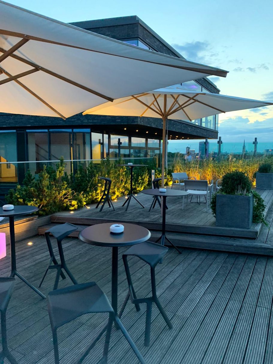 Dachterrasse mit Tischen, Stühlen und Sonnenschirmen bei Dämmerung.