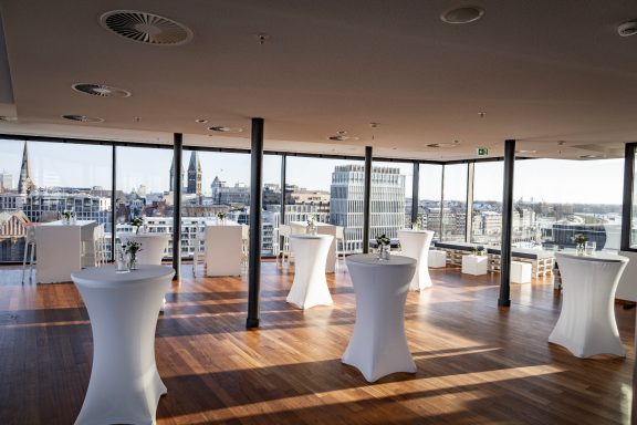Eleganter Eventbereich mit Stehtischen und Blick auf die Stadt.