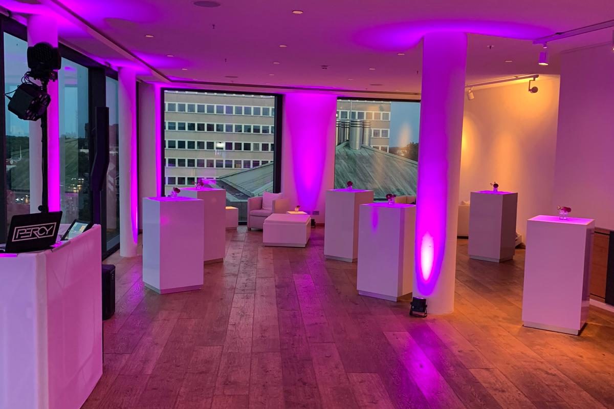 Moderne Eventlocation mit lila Beleuchtung und weißen Möbeln.
