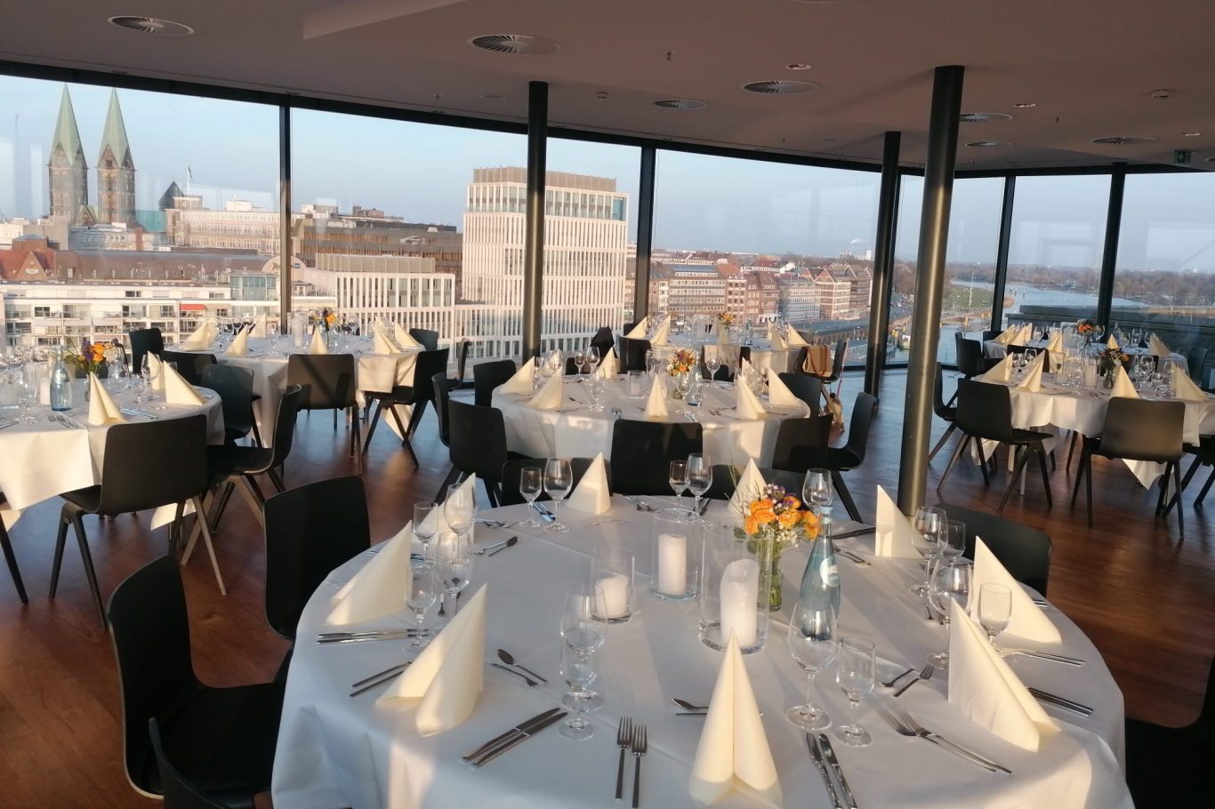 Eleganter Raum mit Blick auf die Stadt, gedeckte Tische und moderne Einrichtung.